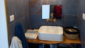 Un bagno con un mobile bagno in legno, un lavandino bianco, un rubinetto dorato, uno specchio e un lampadario a parete.