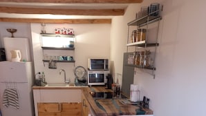 Una cucina accogliente con mobili in legno, un forno a microonde e un lavandino. C'è un divano color petrolio con un cuscino a pois.