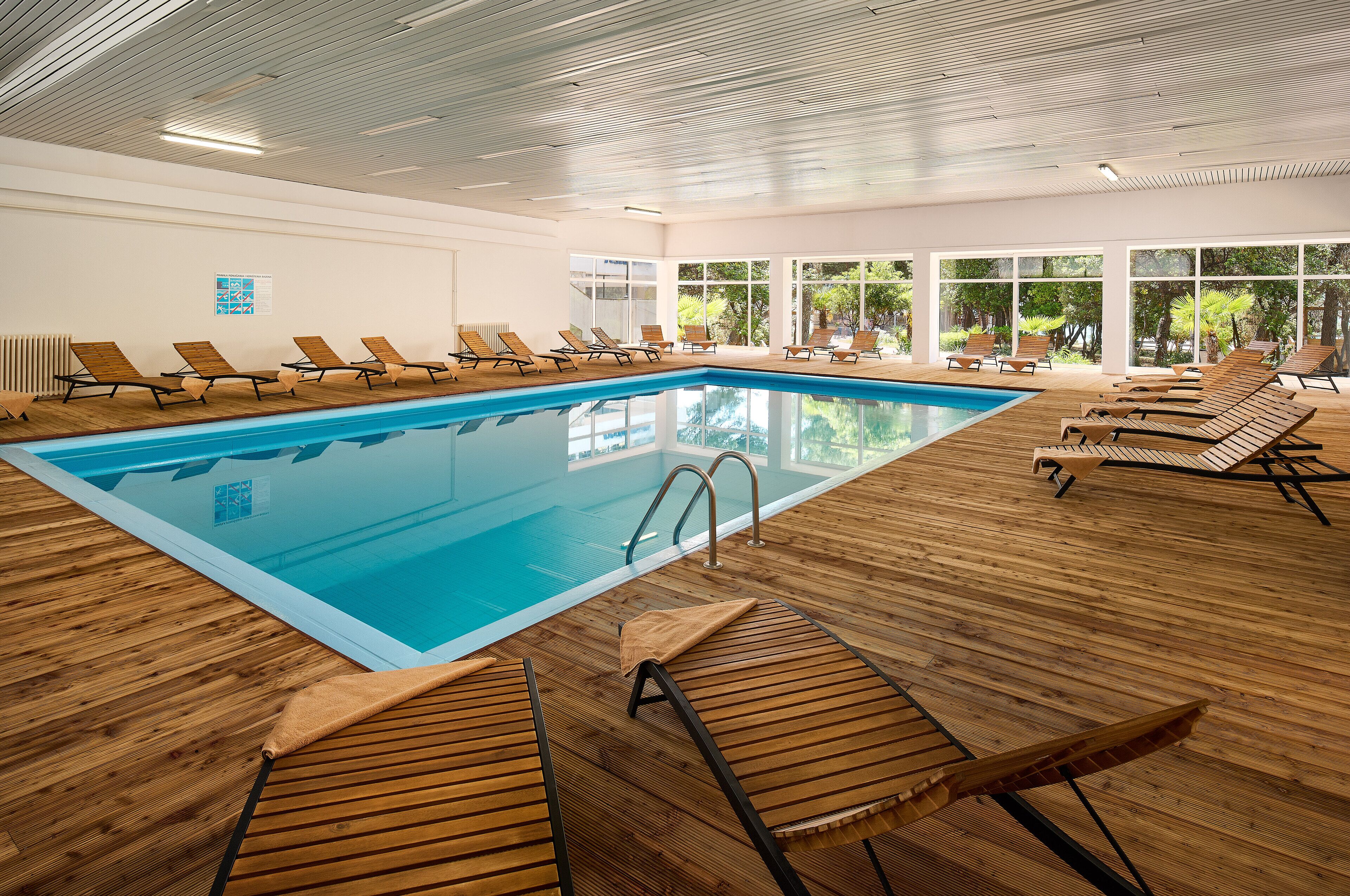 Una piscina coperta con lettini di legno e ampie finestre.