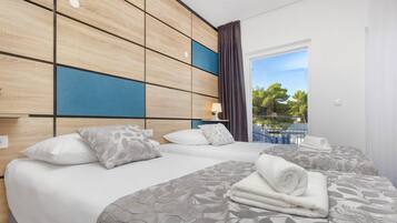 A hotel room with two beds, a wooden headboard, a view of trees through a window, and a balcony.