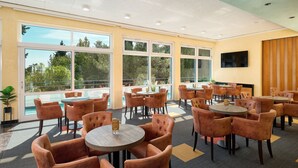 A spacious indoor area with multiple round tables and chairs, large windows offering a view of trees, and a flat-screen TV mounted on the wall. - Ville Imperial Vodice (Vodice)