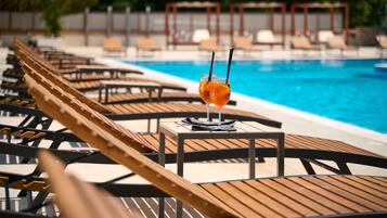 Un espace aménagé au bord de la piscine, avec des chaises longues en bois et une table sur laquelle est posée une boisson.