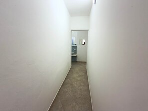 Un pasillo estrecho con paredes blancas y suelo de baldosas que conduce a un baño con lavabo y espejo.