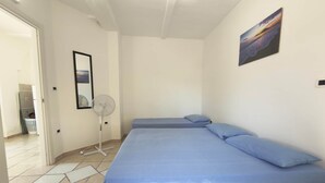 A room with two beds, a standing fan, a door leading to a bathroom, and a painting on the wall.