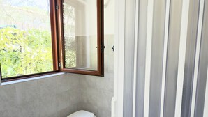 A bathroom with a toilet, a bathtub, a window, and a shower area.