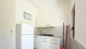 A kitchen with white cabinets, a white refrigerator, a gas stove, and a broom leaning against the wall.