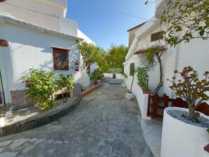 A narrow street with white buildings, potted plants, and a fire extinguisher mounted on a wall. - Villa Maica 6, Palinuro, Cilento (Palinuro)