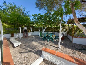 A patio area with a barbecue grill, outdoor seating, and a white wall.