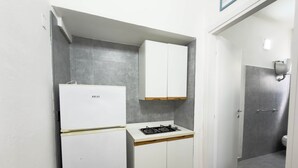 Una cocina compacta con un refrigerador blanco, una estufa a gas y gabinetes blancos.