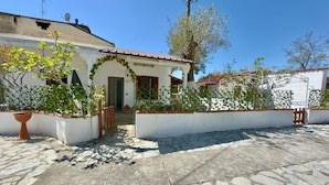 Propiedad residencial con patio de piedra, paredes blancas, techo de tejas rojas y una puerta de madera.