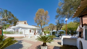 Un patio con un edificio blanco, una zona de estar techada y una palmera.