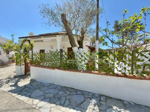 Un edificio blanco con entrada empedrada en piedra, cerca blanca y un árbol de hojas verdes.