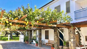A covered outdoor area with a pergola, stone pillars, potted plants, and a white building with a balcony. - Villa Arco 1, Palinuro, Cilento (Palinuro)