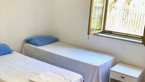 A small, clean room with two single beds, a small bedside table, and a window with a view of a fence and trees. - Villa Arco 1, Palinuro, Cilento (Palinuro)