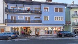A multi-story building with a ground-floor shop, balconies, and parked cars.