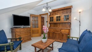 A living room with a television, wooden cabinets, a sofa, and a table with a vase of flowers.