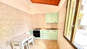 A compact kitchen with a dining area, featuring a gas stove, sink, and light green cabinets. - Villa Arco 4, Palinuro, Cilento (Palinuro)