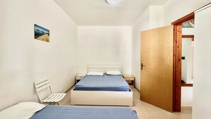 A small, clean room with a bed, a chair, and a wooden door. - Villa Arco 4, Palinuro, Cilento (Palinuro)