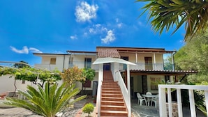 A two-story house with a staircase leading to a balcony, surrounded by potted plants and a patio area. - Villa Arco 7, Palinuro, Cilento (Palinuro)
