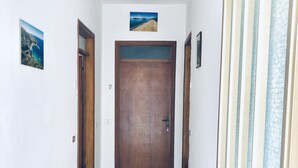 Een gang met een houten deur, betegelde vloer en een klein, ingelijst fotootje aan de muur.