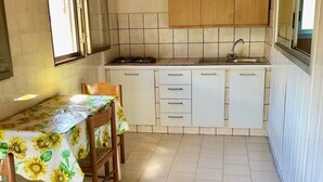 Cozinha com armários brancos, fogão a gás e pia. Há uma mesa de jantar com cadeiras e uma janela acima.
