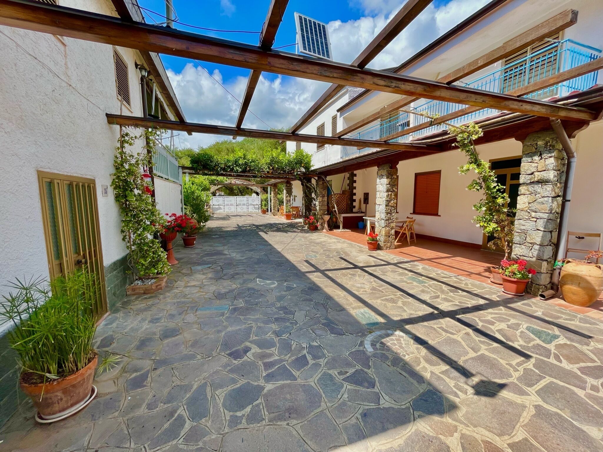 A courtyard with stone flooring, potted plants, and a wooden pergola structure.