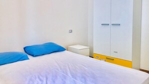 A bedroom with a bed, two blue pillows, a white bedside table, and a large wardrobe with a yellow lower section. - Villa Arco 2, Palinuro, Cilento (Palinuro)