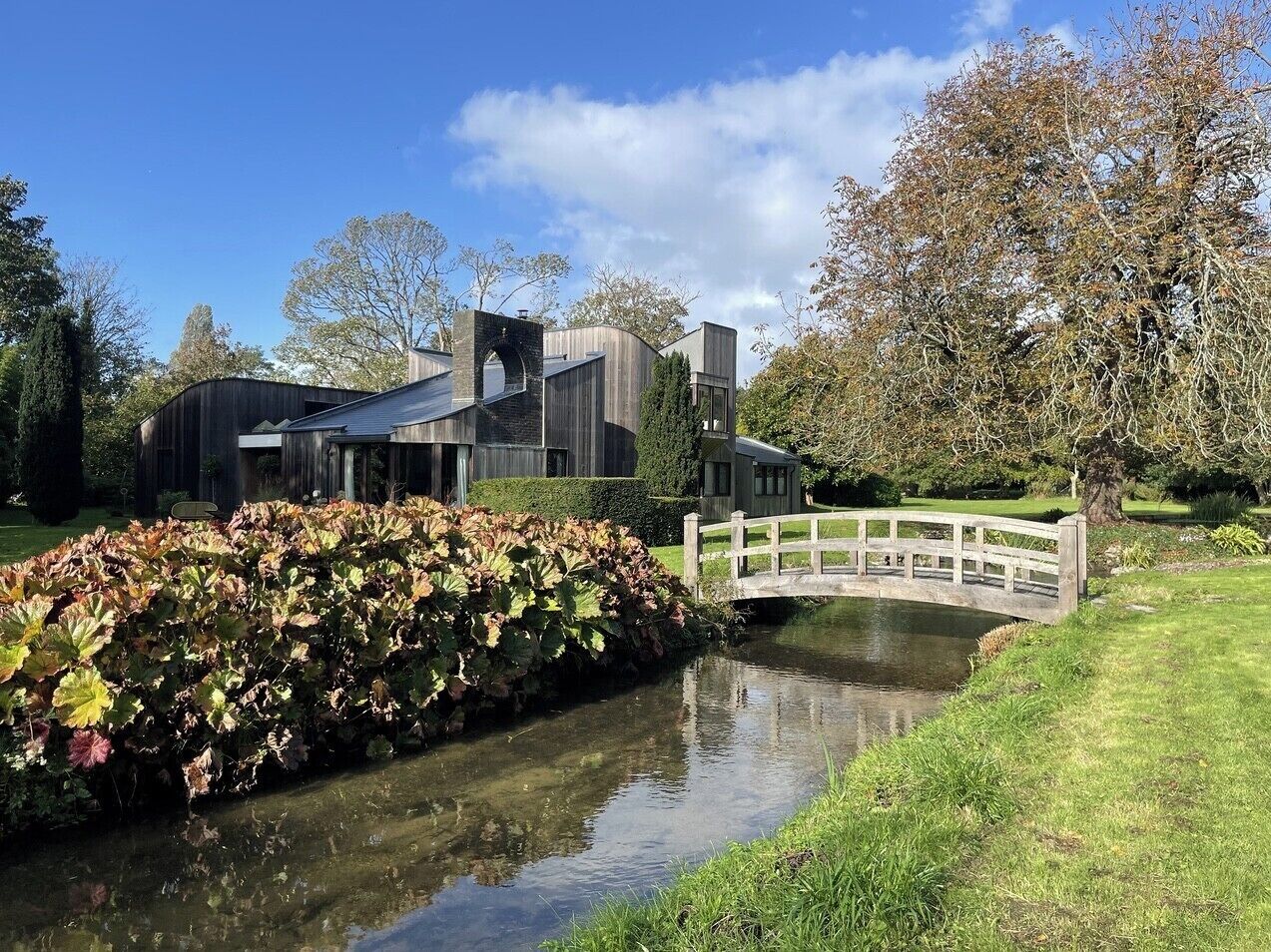 A modern building with a large glass facade, a small bridge, and a canal with water plants.