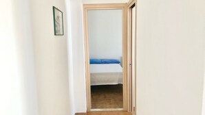 A narrow hallway leading to a bedroom with a bed and a wooden door. - Villa Arco 9, Palinuro, Cilento (Palinuro)