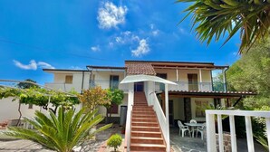 A two-story house with a staircase leading to a balcony, surrounded by potted plants and a patio area. - Villa Arco 9, Palinuro, Cilento (Palinuro)