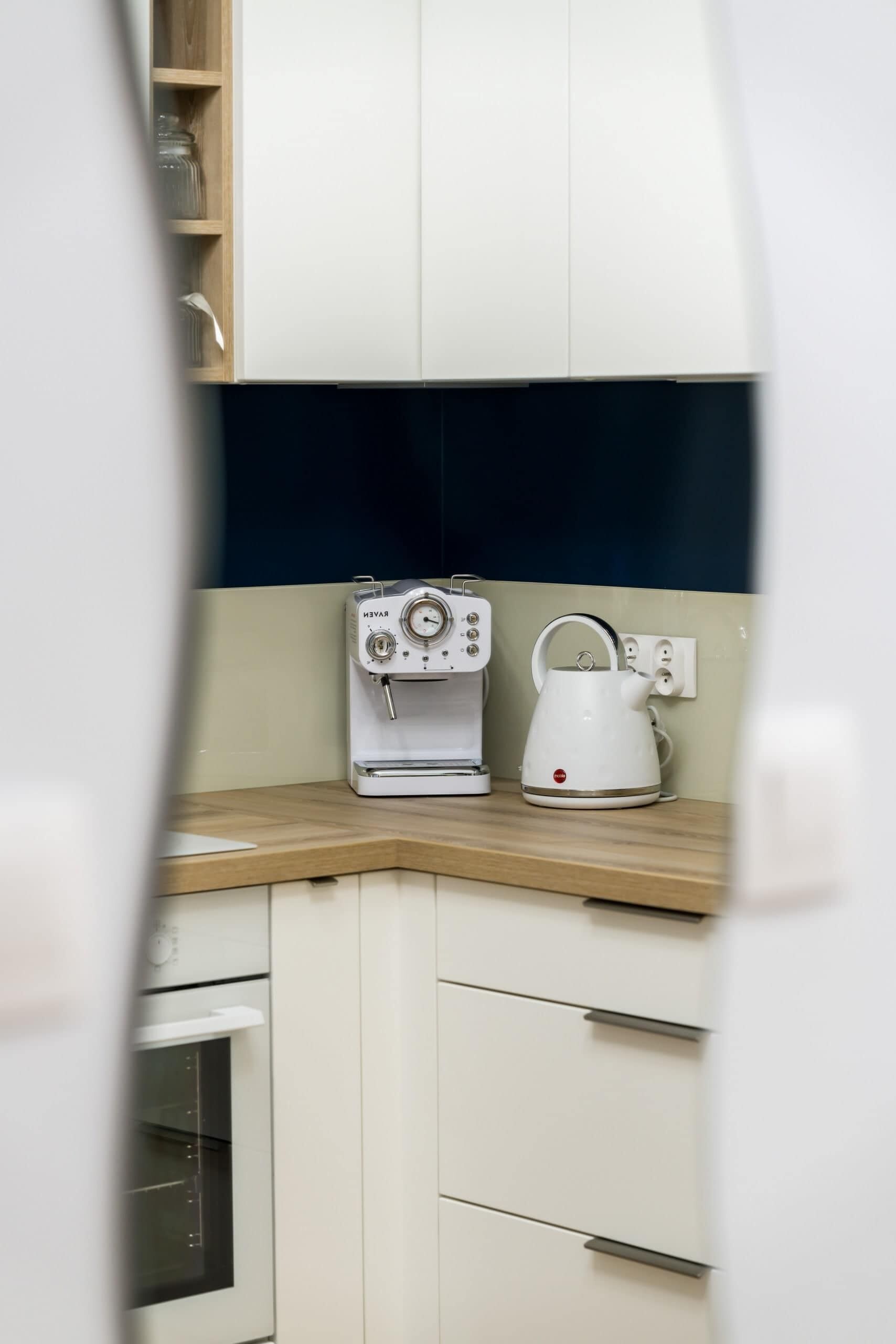 A kitchen with white cabinets, a coffee maker, and a kettle on the countertop.