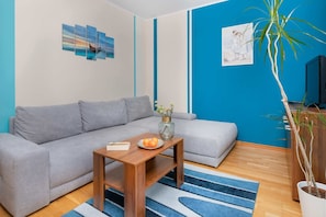 A living room with a grey sofa, a wooden coffee table, a vase with flowers, a blue and white striped rug, and a large potted plant.