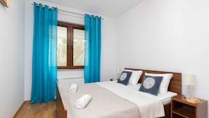 Ein ordentlich gemachtes Bett mit einer weiß-beigen Karodecke, zwei Kissen und zwei aufgerollten Handtüchern.