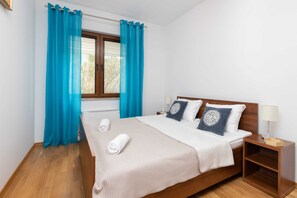 A neatly made bed with a white and beige checkered bedspread, two pillows, and two rolled towels.