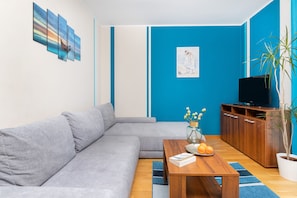 A living room with a grey sofa, a wooden coffee table, a blue wall, and a TV stand.