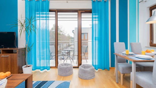 Ein modernes Wohnzimmer mit Fernseher, Sitzgelegenheiten, einem Essbereich und einem Balkon mit blauen Vorhängen.