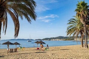 A beach with palm trees, beach chairs, and umbrellas.