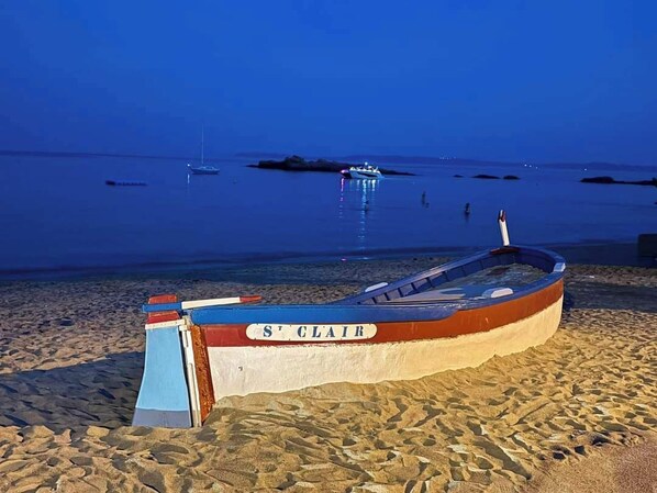 A boat named "St Clair" on a sandy beach with calm water and a few boats in the distance.
