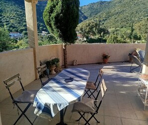 A patio with a table and chairs, potted plants, and a view of a mountainous landscape.