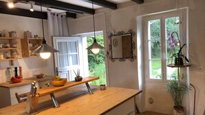 Eine Küche mit Holzarbeitsplatten, einer zentralen Kochinsel, hängenden Pendelleuchten und einem Fenster mit Blick auf Grünflächen.