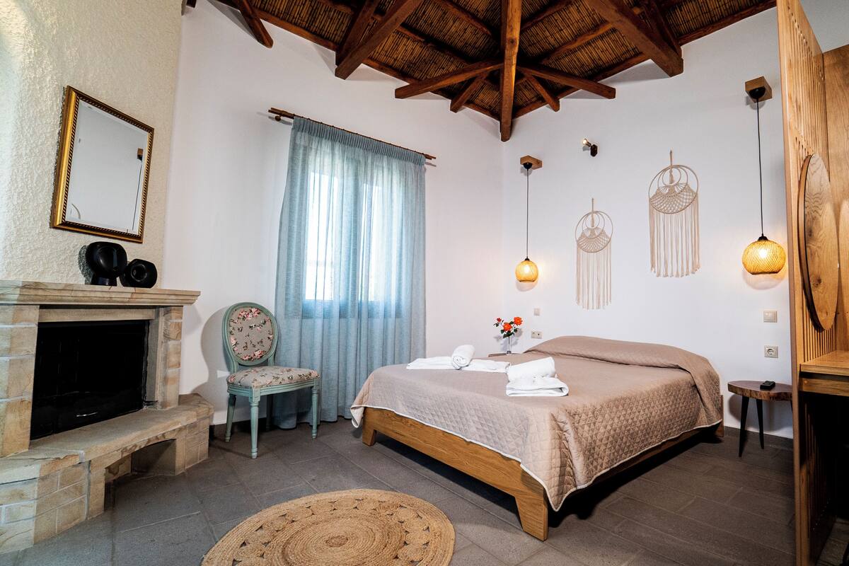 A bedroom with a bed, a chair, a fireplace, and a hanging light fixture.