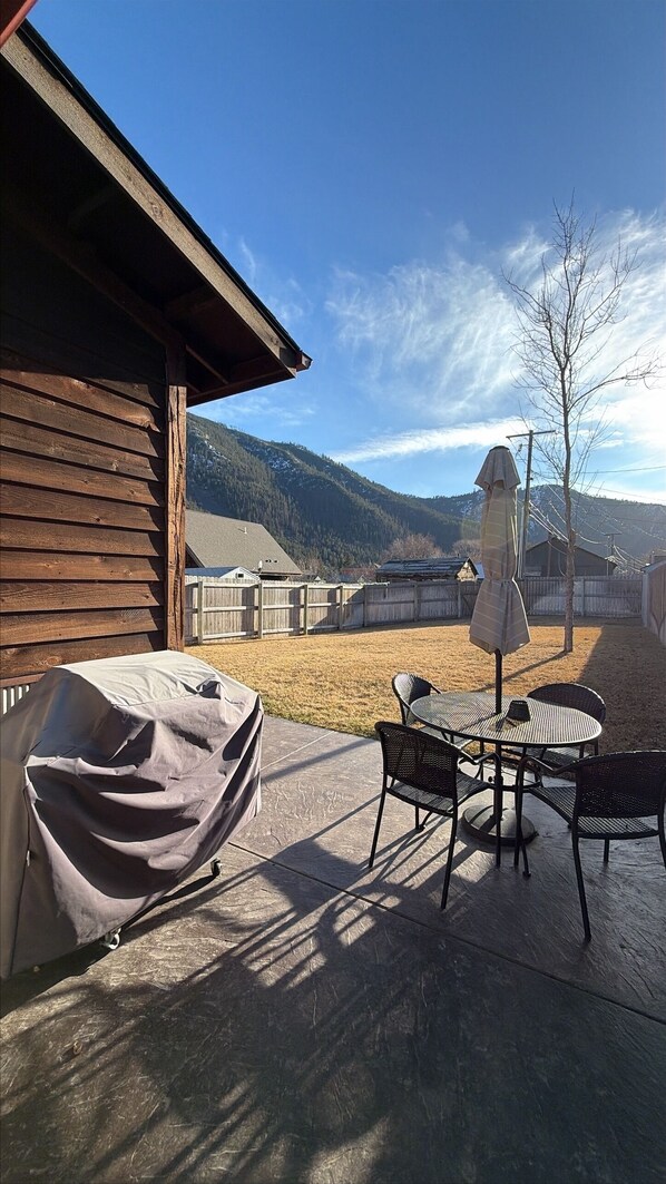 An outdoor patio with a covered grill, a table, and chairs.