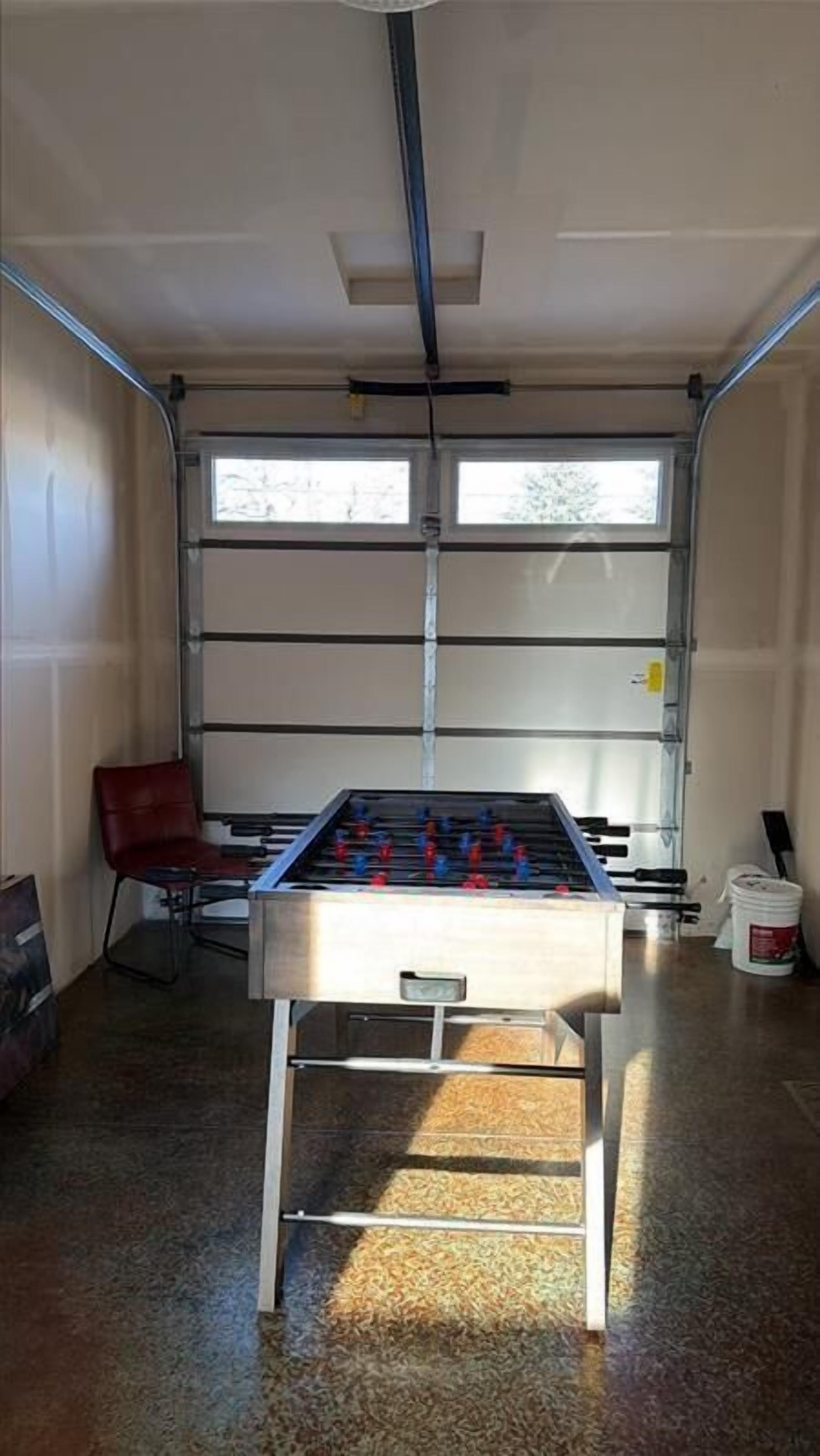 A room with a foosball table, a red chair, and a window with blinds.