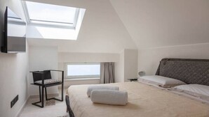 A bedroom with a skylight, a bed with white linens, a chair, and a bedside table. - Apartment Ogliarola - Maina Country Resort - with pool, in Sicily (Cresta)
