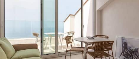 A balcony with a glass door, a round table with chairs, and a green sofa.