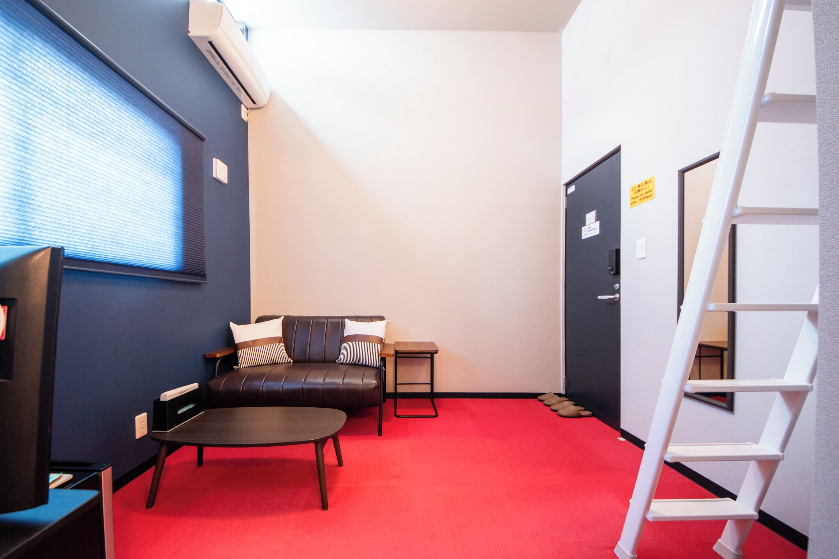 A compact living space with a red carpet, a leather sofa, a small table, and a white ladder.