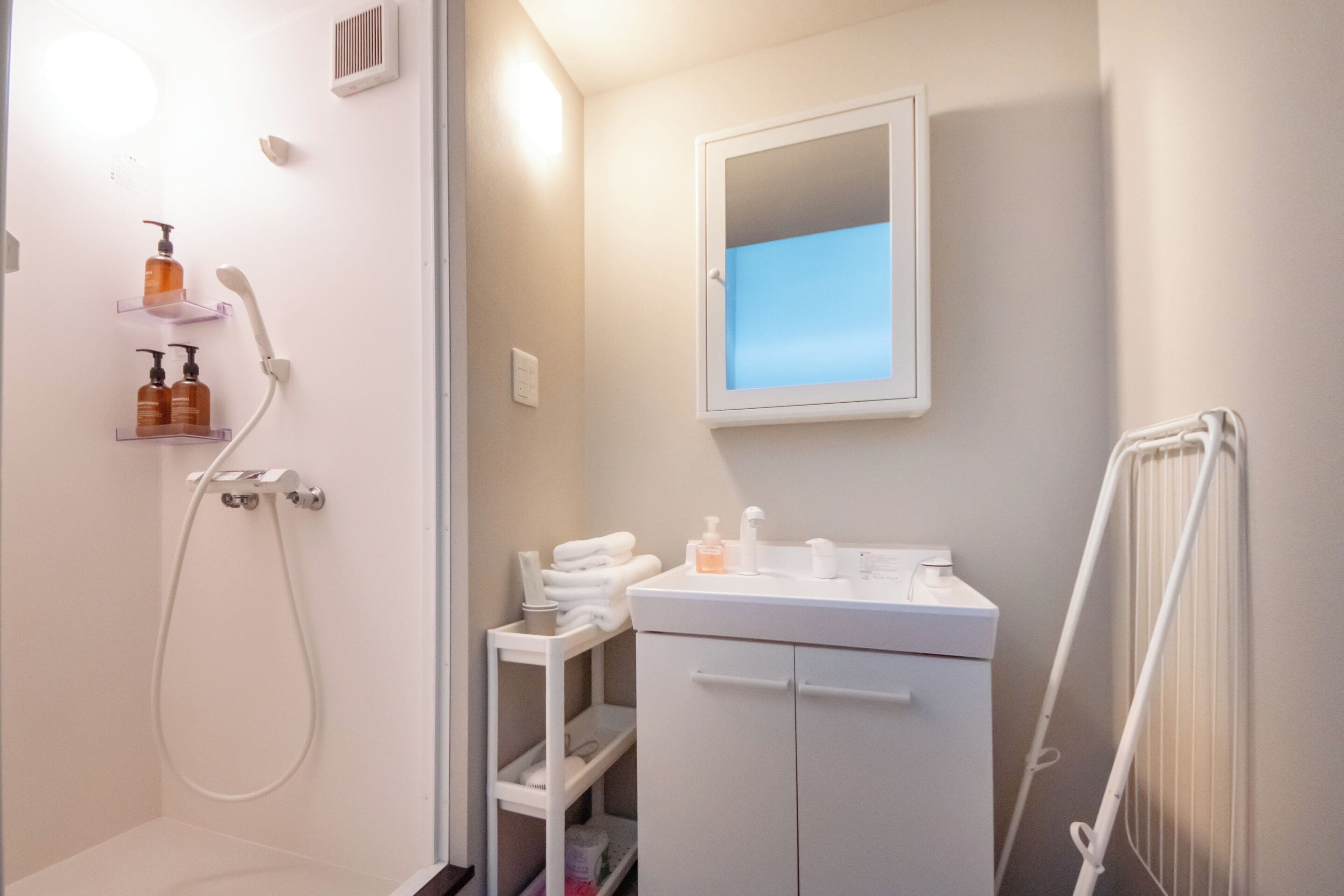 A bathroom with a shower, a sink, and a mirror. There are toiletries on the sink and a towel rack.