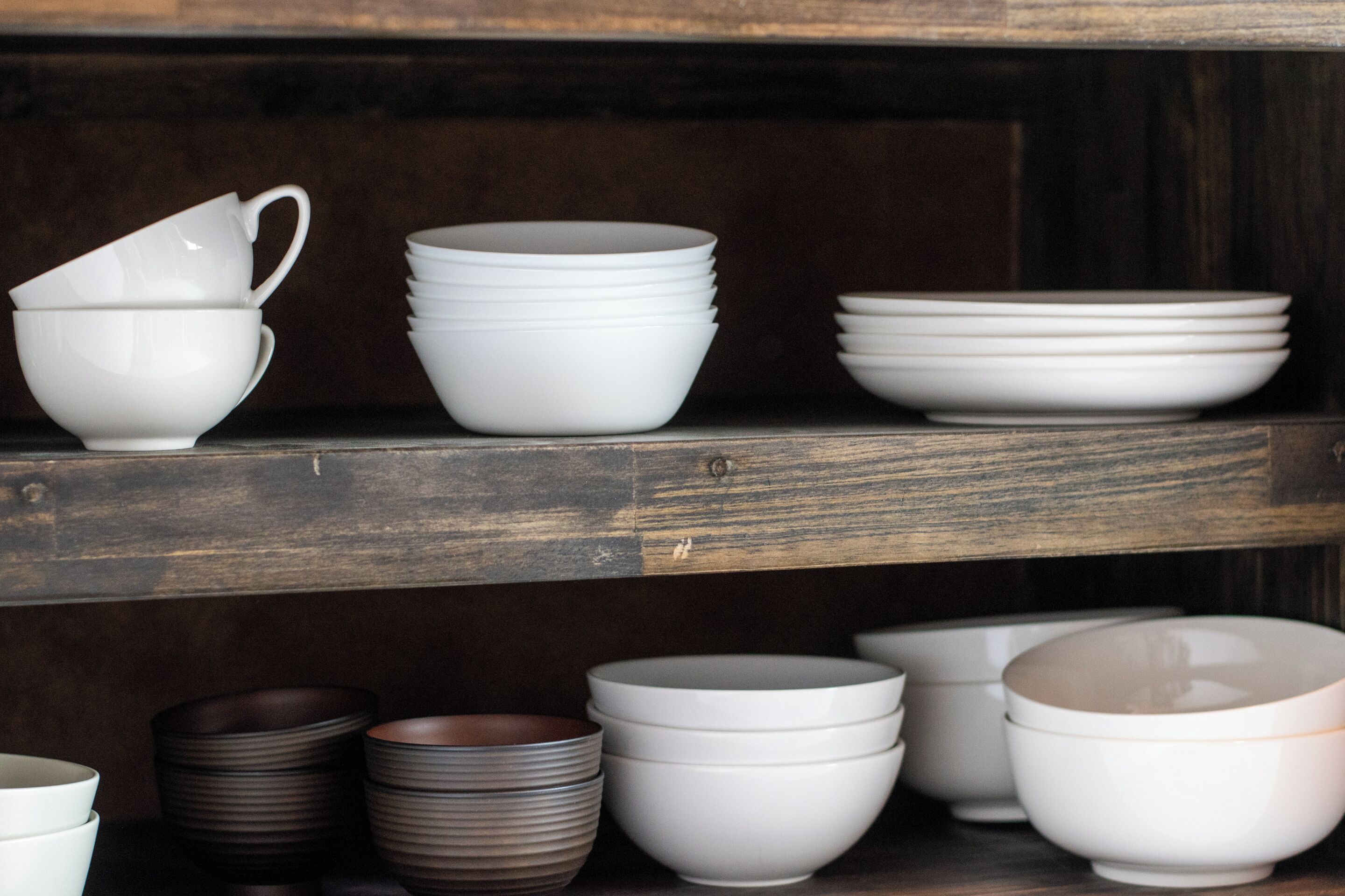 A wooden shelf with white and brown bowls and plates.