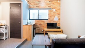 A compact room with a wooden wall, a sink, a television, a bed, and a small table.