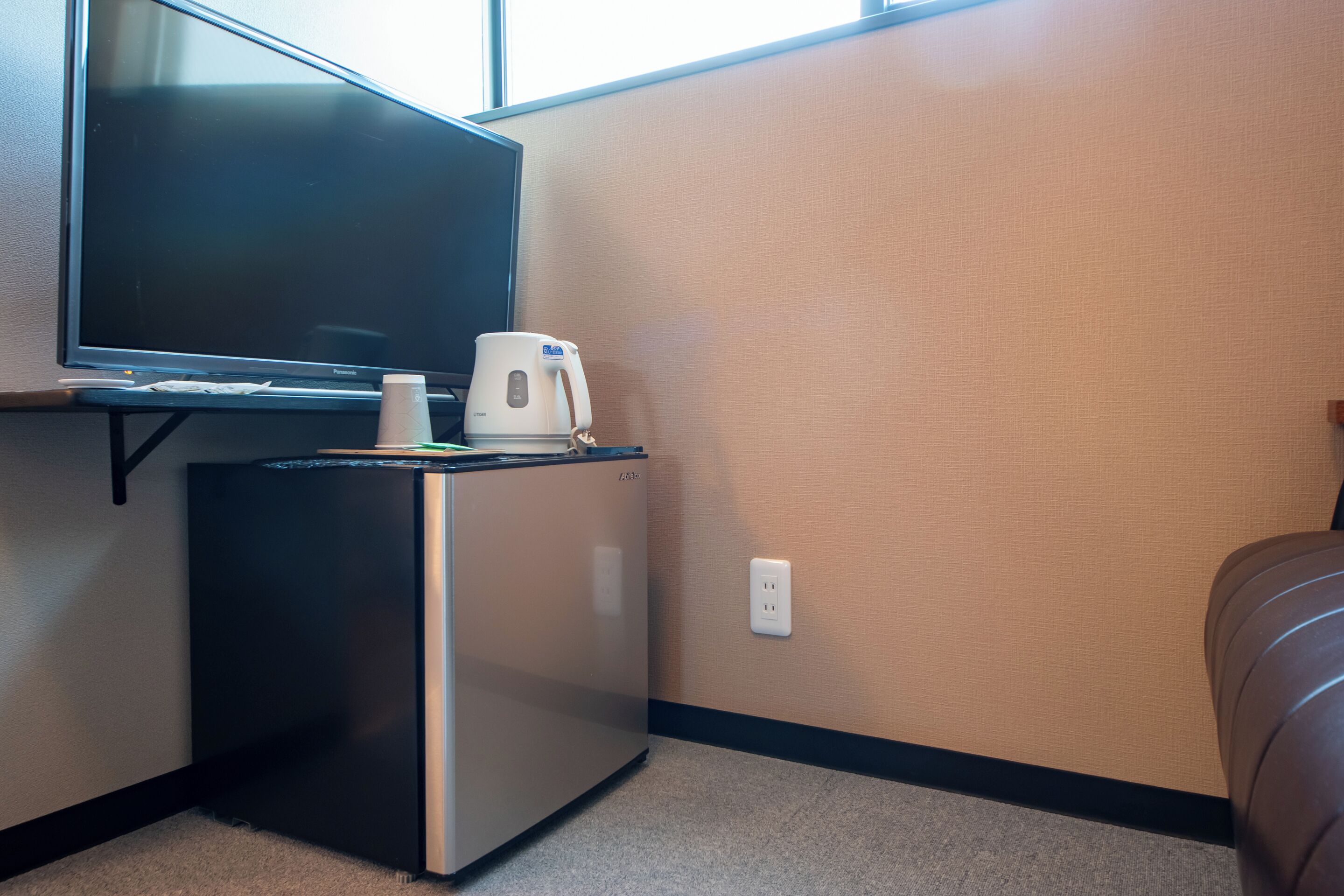 A compact kitchenette with a refrigerator, a coffee maker, and a flat-screen TV on a stand.